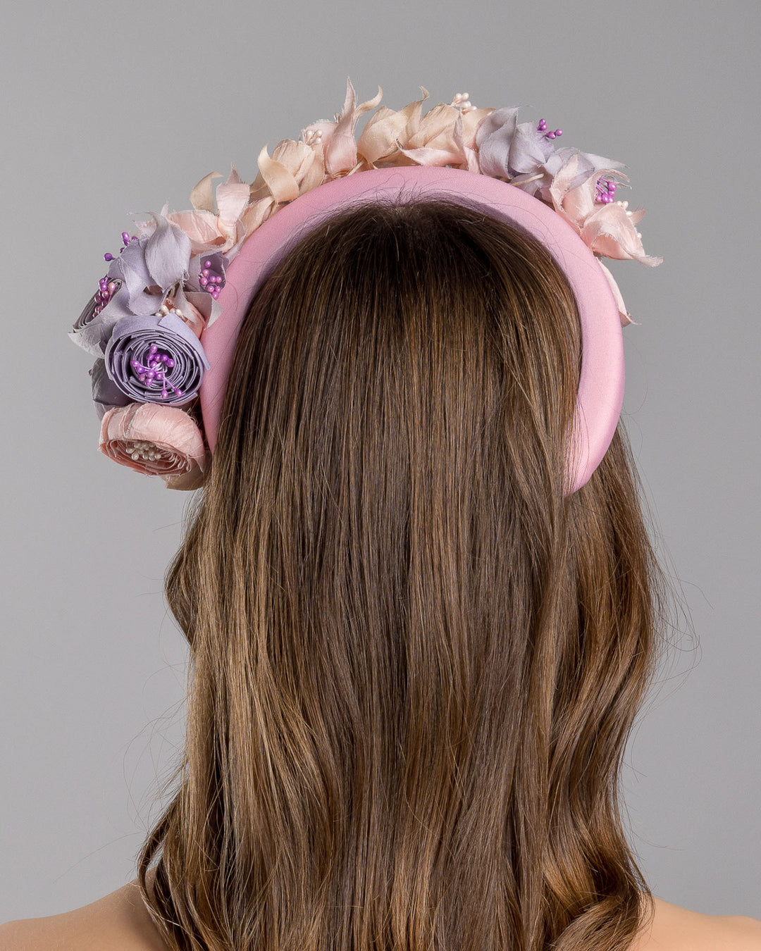 Model showcasing the back side close up of high pink headband decorated with custom made silk taffeta lilac, pink and ecru bouquet of peony and fuchsia flowers. Made by Merve Bayindir.