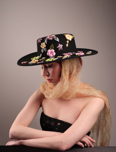 The female model is wearing a wool felt wide-brimmed boater hat showcasing the multi-colour satin embroidery flower details on the right side of the hat, as well as an organza long scarf that falls from both sides. Designed by Merve Bayindir.