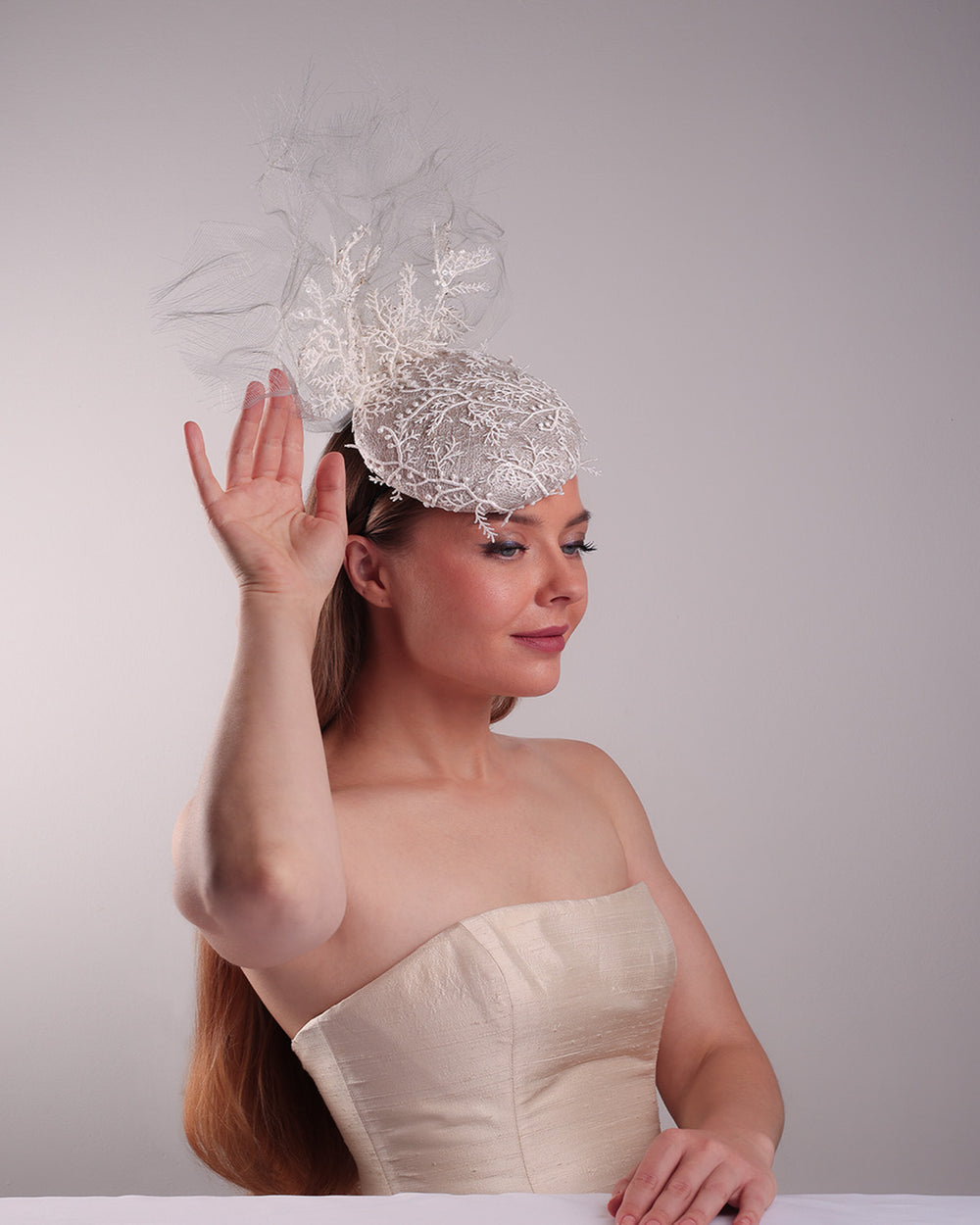 Model is showcasing the right front part of a grey button shaped fascinator, fully covered with white branch look designed 3D lace with movement. Embellished with a grey crinoline cloud detaling a wired lace pieaces looking like branches. Fitted with a wire heaband and elastic.