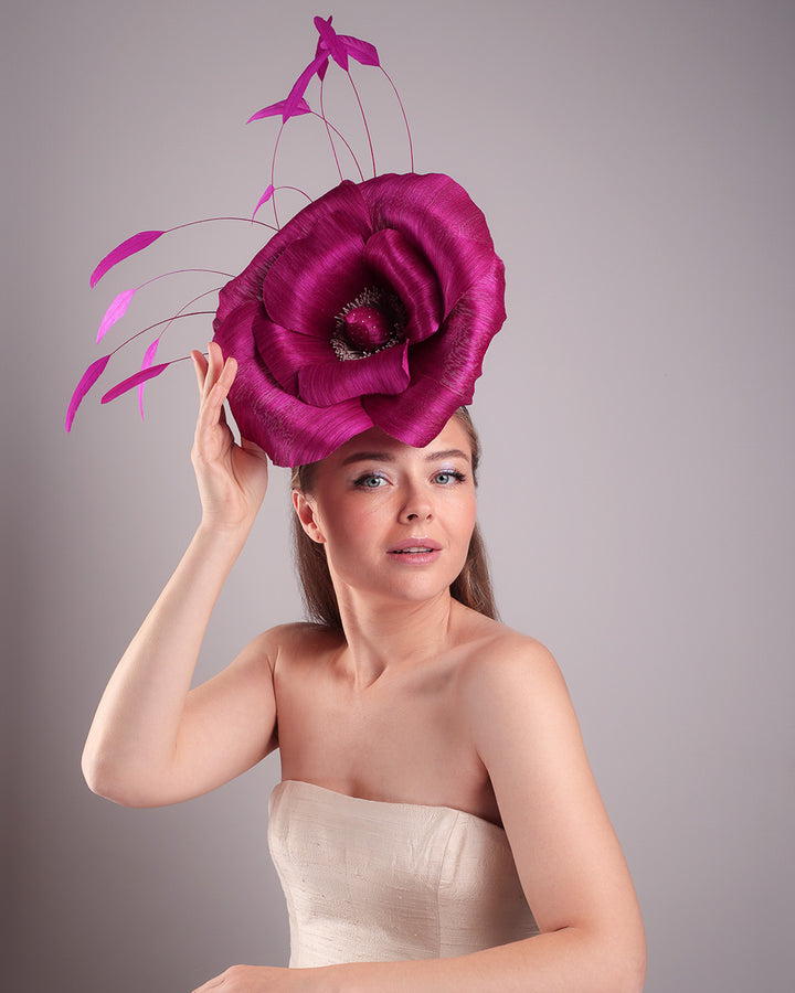 Model is showcasing the left  front angle of large fascinator adorned with a fuchsia hand-made silk-abaca large flower, placed on a lilac coloured mini saucer. The mini saucer base is fixed on a custom headband and secured with an additional elastic.