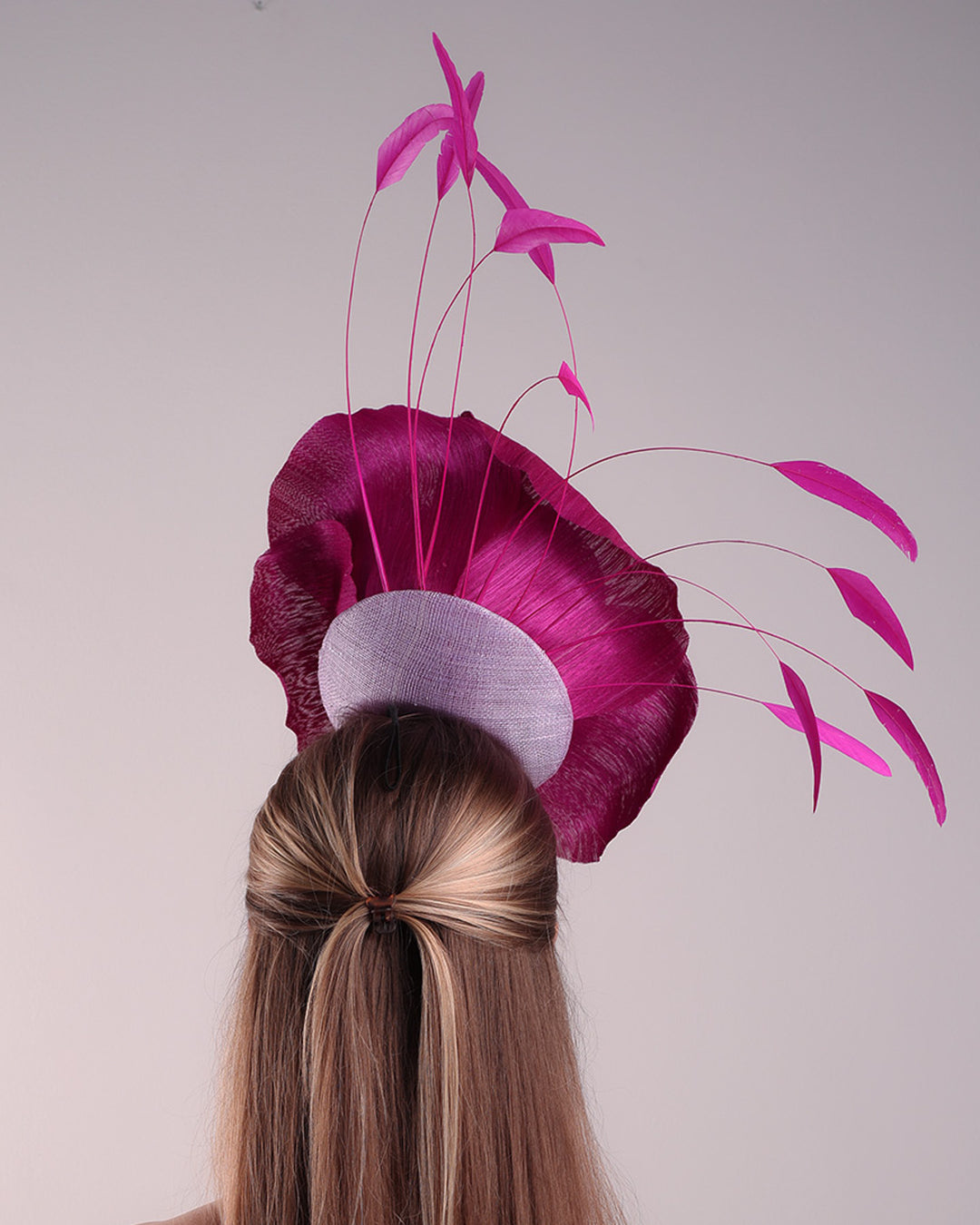 Model is showcasing the back of a large fascinator adorned with a fuchsia hand-made silk-abaca large flower, placed on a lilac coloured mini saucer. The mini saucer base is fixed on a custom headband and secured with an additional elastic.