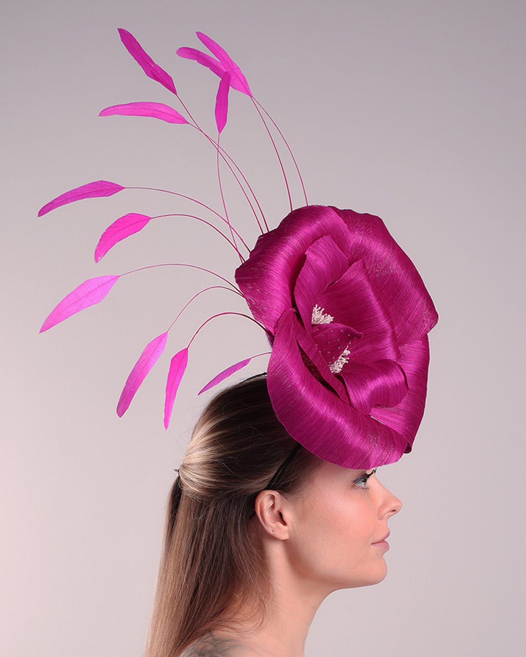 Model is showcasing right side of a large fascinator adorned with a fuchsia hand-made silk-abaca large flower, placed on a lilac coloured mini saucer. The mini saucer base is fixed on a custom headband and secured with an additional elastic.