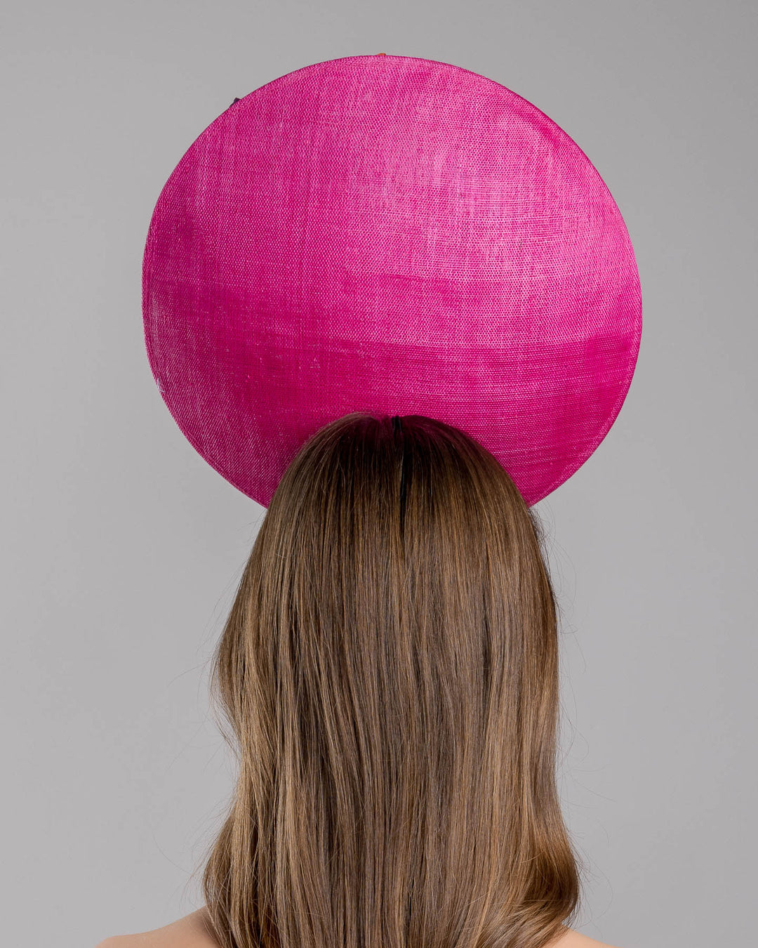 The model is showcasing the back side close up of the large size oval shaped hot pink fascinator decorated with custom made silk organza multi-coloured violets. Designed and made by Merve Bayindir Millinery.
