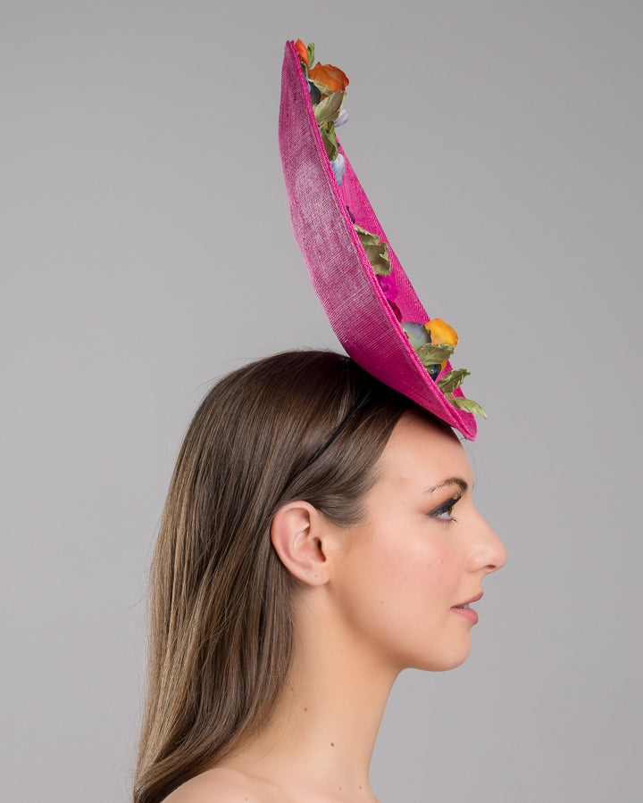 The model is showcasing the right side close up of the large size oval shaped hot pink fascinator decorated with custom made silk organza multi-coloured violets. Designed and made by Merve Bayindir Millinery.
