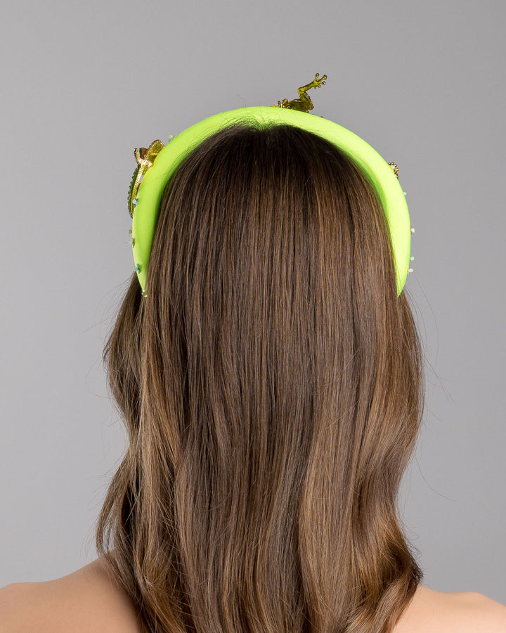 Model is showcasing back side close up of the florescent green high headband embroidered with multi colour flower sequins decorated with two multi colour crystal embellished frog brooches and a multi-colour crystal decorated chameleon. Made by Merve Bayindir Millinery.