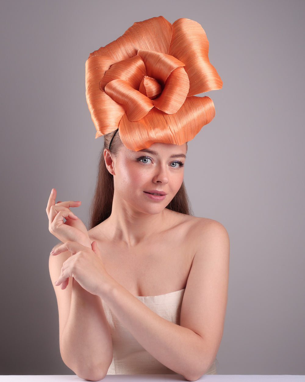 Model is show casing the front of a large peach orange coloured hand-made silk abaca flower, secured with a headband and an additional elastic. The peach fascinator is perfect for events like Royal Ascot or Kentucky.