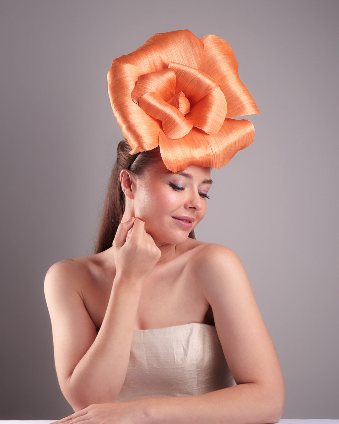 Model is showcasing a front right side of a large peach orange coloured hand-made silk abaca flower, placed on a sky blue mini saucer. The mini saucer base is fixed on a custom headband and secured with an additional elastic. The peach fascinator is perfect for events like Royal Ascot or Kentucky.