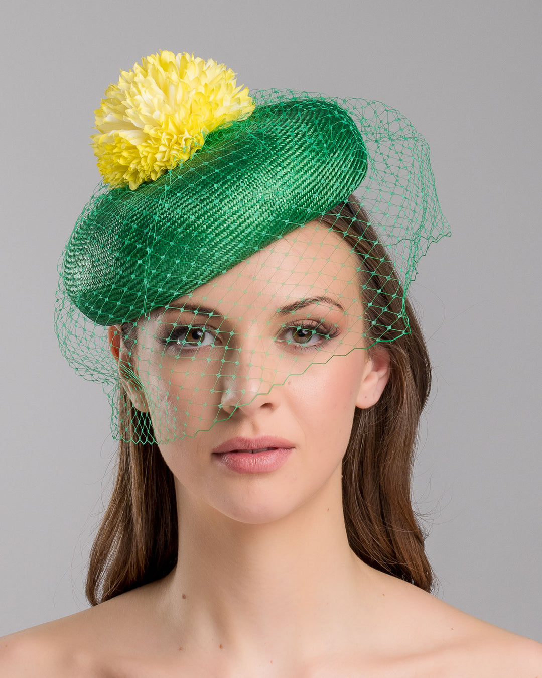 Model is showcasing the front side close up of green summer beret tilted to the right side of the head, the vibrant headpiece is rounded with a delicate emerald green veil and completed with a bright yellow pompom flower on top. Designed and made by Merve Bayindir millinery.