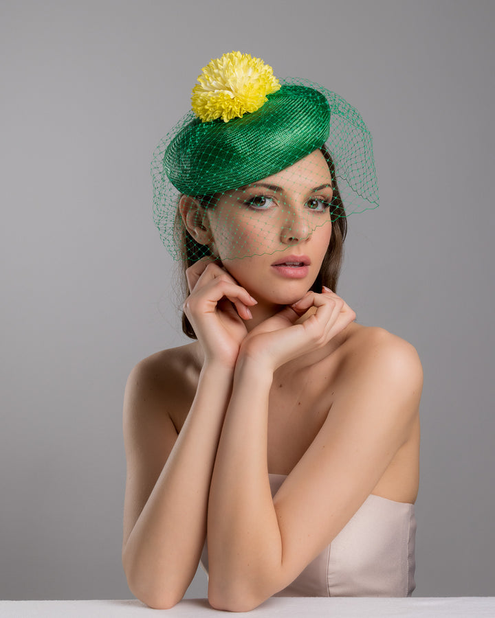 Model is posing wearing the Gray green summer beret tilted to the right side of the head, the vibrant headpiece is rounded with a delicate emerald green veil and completed with a bright yellow pompom flower on top. Designed and made by Merve Bayindir millinery.