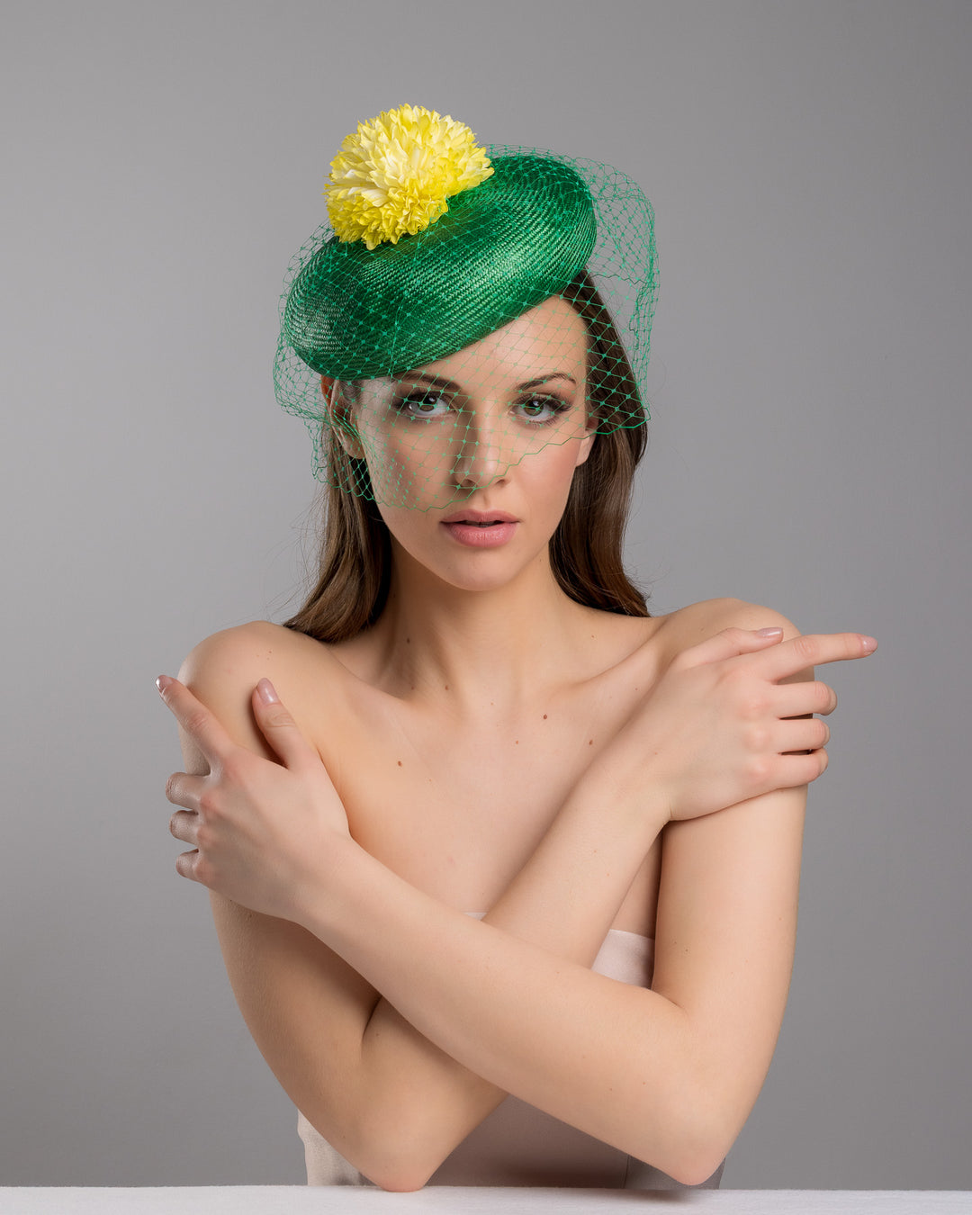 Model is posing wearing the Gray green summer beret tilted to the right side of the head, the vibrant headpiece is rounded with a delicate emerald green veil and completed with a bright yellow pompom flower on top. Designed and made by Merve Bayindir millinery.