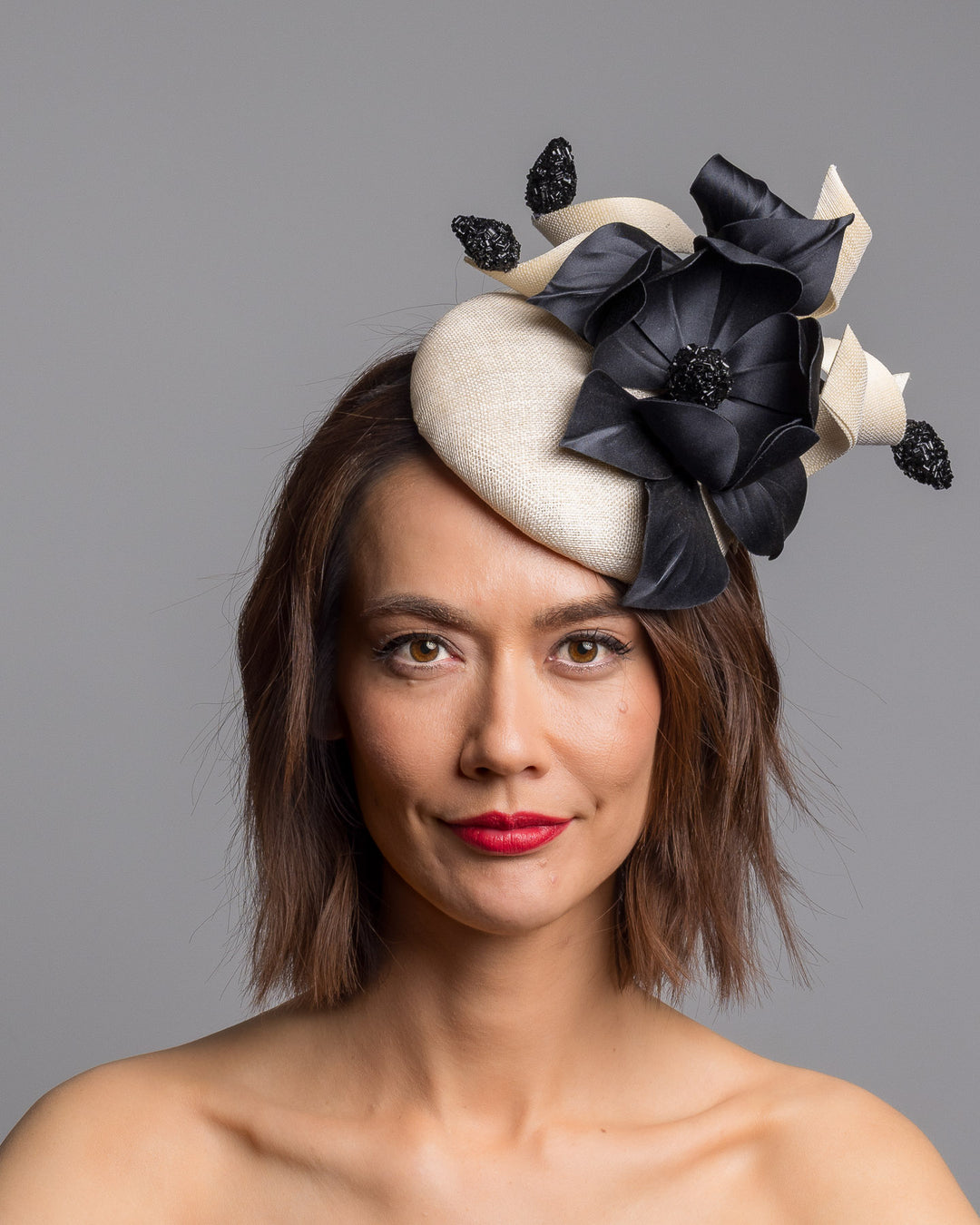 The model is showcasing the front side close up of the grade sinamay button shaped white fascinator decorated with white Jinsin Swirls and custom made black American Sateen Cala flower. Designed and made by Merve Bayindir Millinery.

