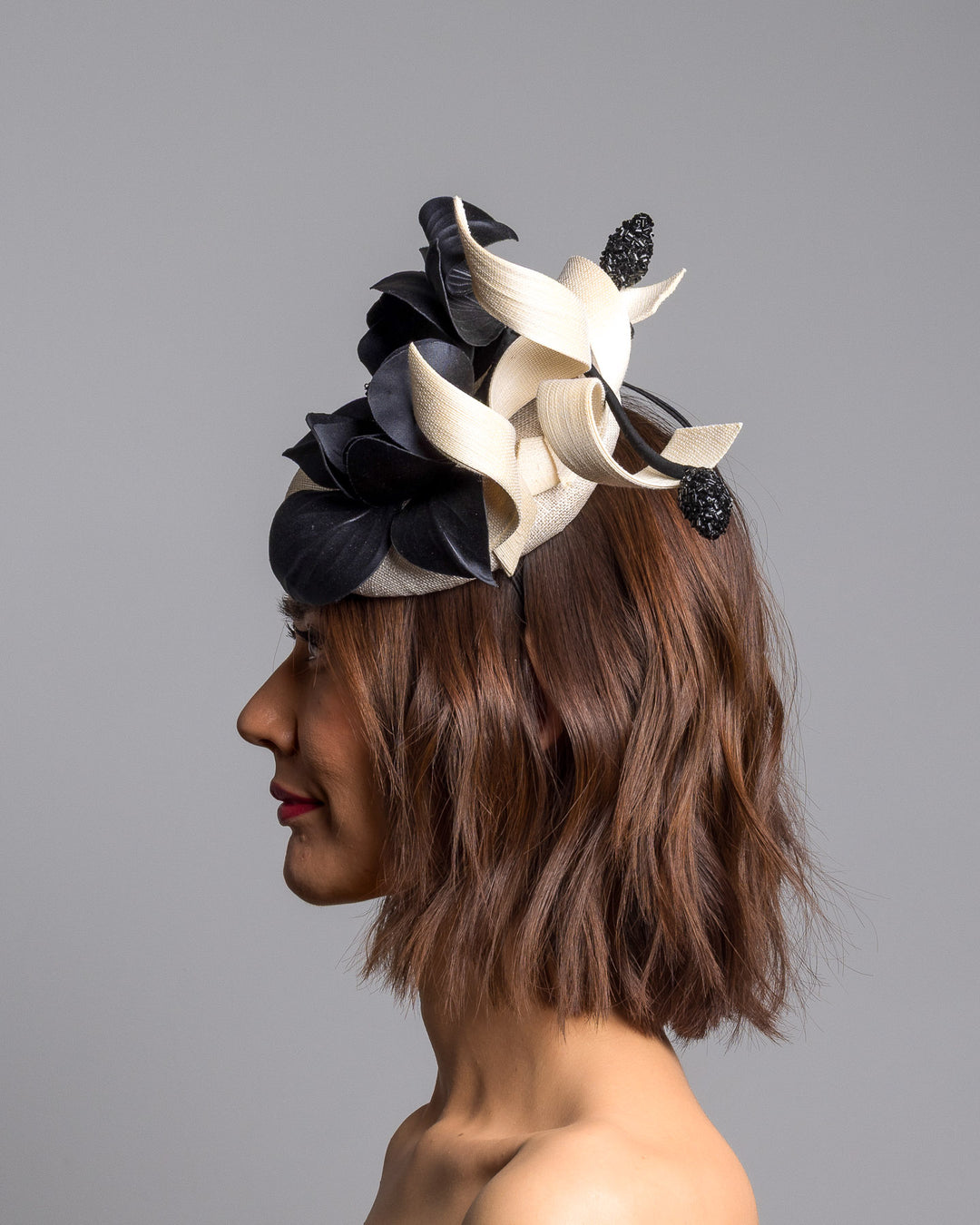 The model is showcasing the left side close up of the grade sinamay button shaped white fascinator decorated with white Jinsin Swirls and custom made black American Sateen Cala flower. Designed and made by Merve Bayindir Millinery.

