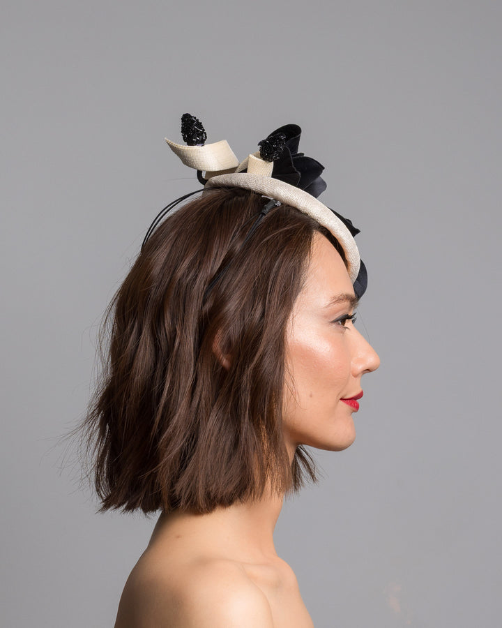 The model is showcasing the right side close up of the grade sinamay button shaped white fascinator decorated with white Jinsin Swirls and custom made black American Sateen Cala flower. Designed and made by Merve Bayindir Millinery.


