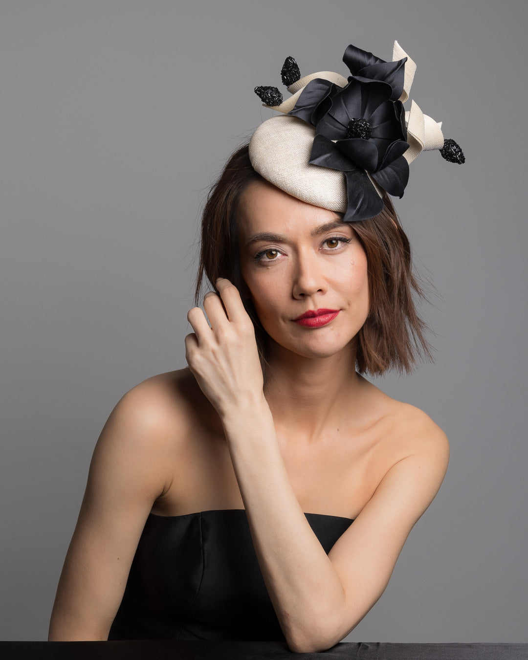 The female model is posing, wearing 
Guinea,the grade sinamay button shaped white fascinator decorated with white Jinsin Swirls and custom made black American Sateen Cala flower. Designed and made by Merve Bayindir Millinery.
