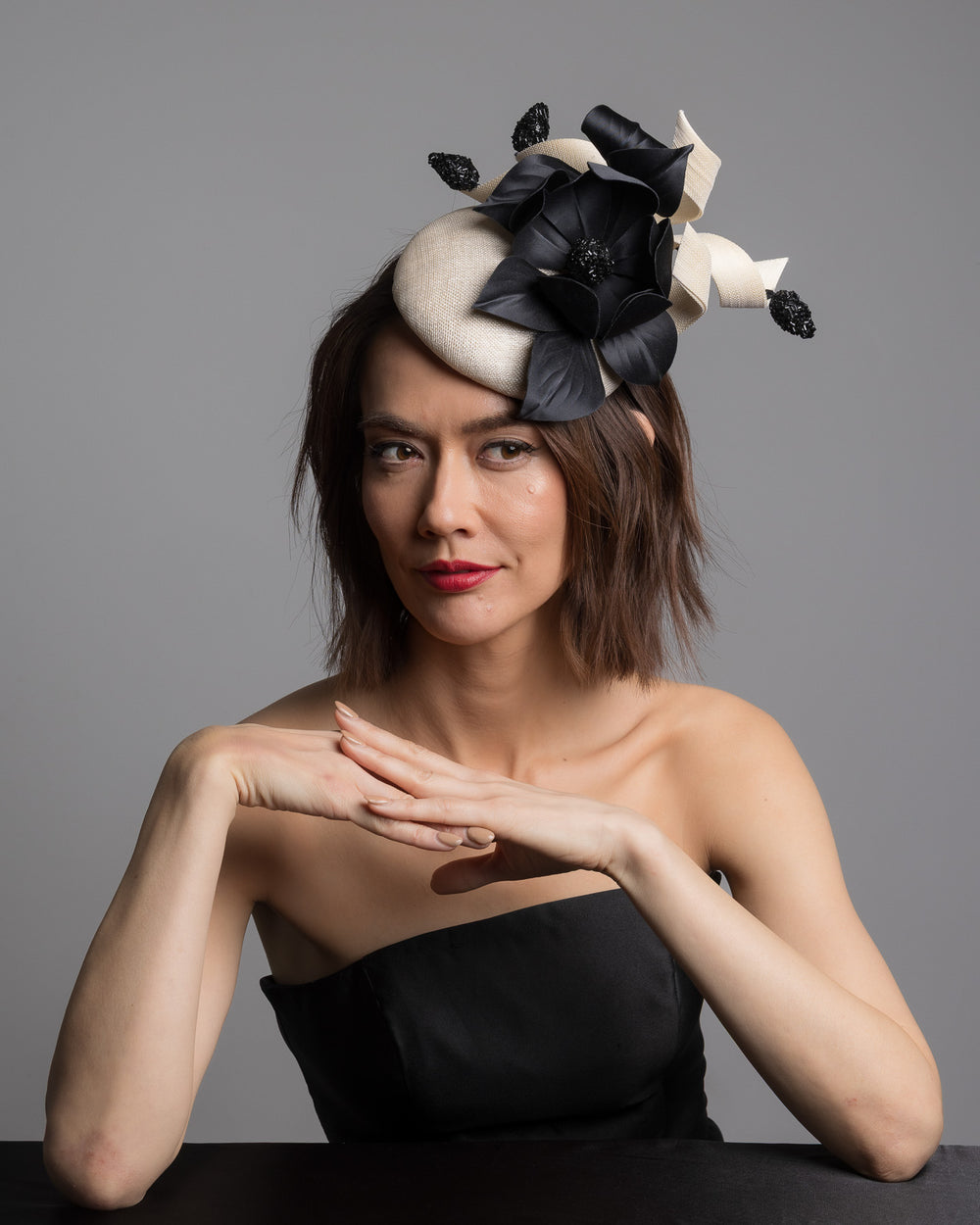 The female model is posing, wearing 
Guinea,the grade sinamay button shaped white fascinator decorated with white Jinsin Swirls and custom made black American Sateen Cala flower. Designed and made by Merve Bayindir Millinery.
