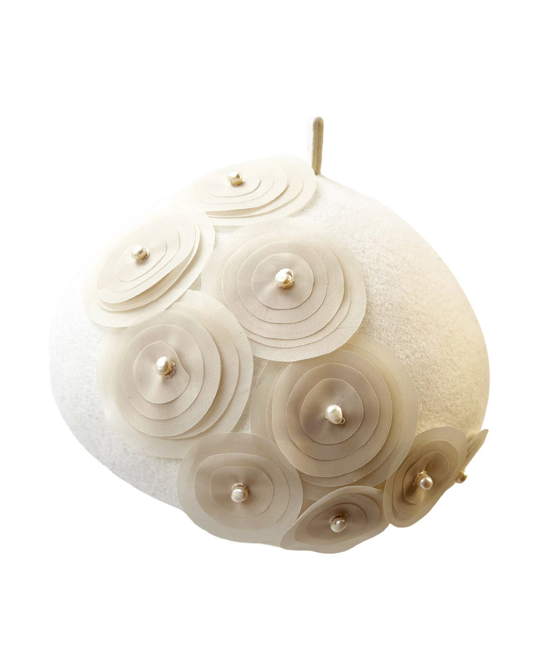Still life picture of the Heaven pillbox beret hat, crafted in soft white felt and adorned with swirling ivory appliqué rosettes of different sizes and layers, each hand-finished with a delicate pearl. Designed by Merve Bayindir.