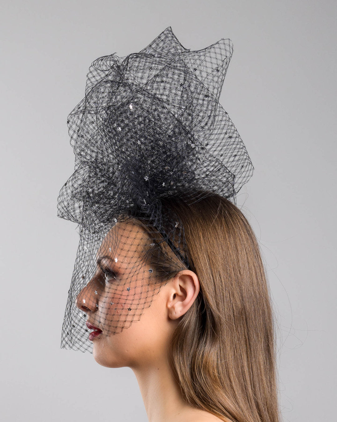 Model is showcasing the left side of the Hera Fascinator made with custom three leg headband covered with double-threaded veil, embroidered with silver stars by Merve Bayindir millinery.