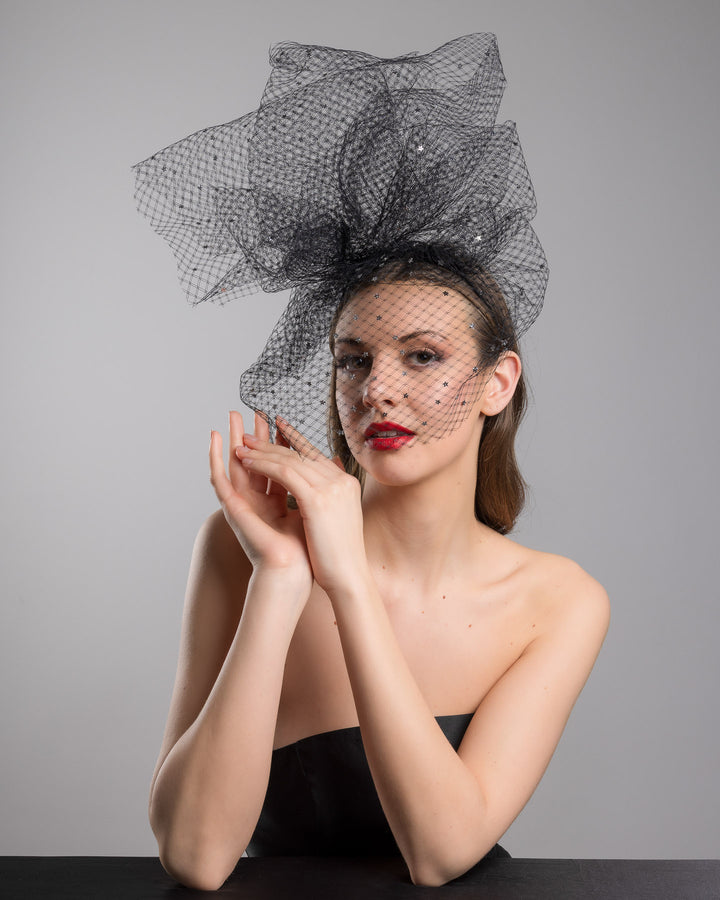 Model is posing wearing the Hera Fascinator made with custom three leg headband covered with double-threaded veil, extending like a cloud, embroidered with silver stars by Merve Bayindir millinery.