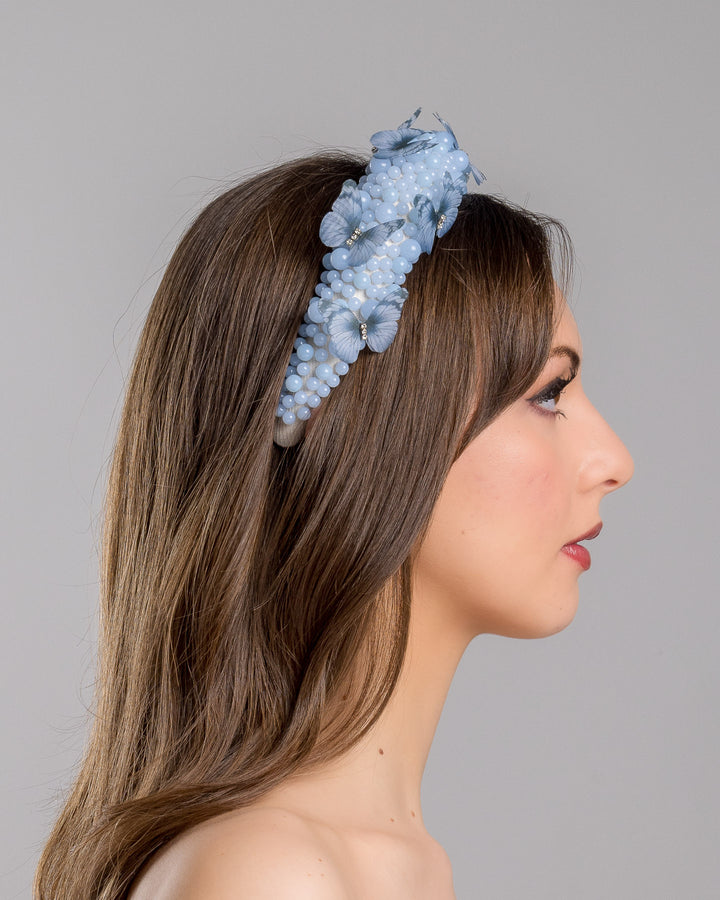 Model is showcasing the right side close up of high headband decorated with different sized mat blue beads and scattered blue organza butterflies with crystal centres. Made by Merve Bayindir millinery.