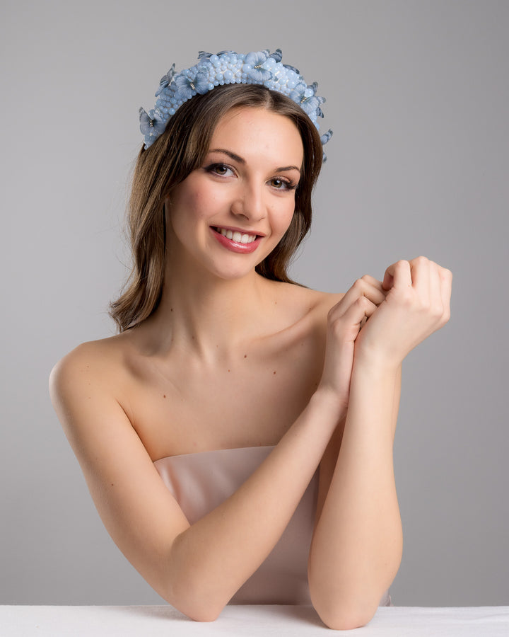 Female model is posing wearing Ice high headband decorated with different sized mat blue beads and scattered blue organza butterflies with crystal centres. Made by Merve Bayindir millinery.