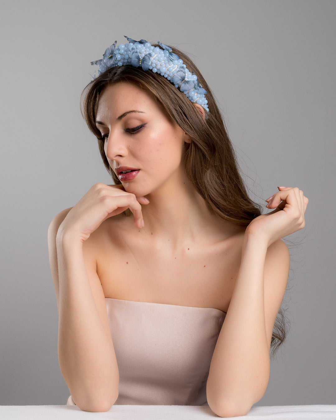 Female model is posing wearing Ice high headband decorated with different sized mat blue beads and scattered blue organza butterflies with crystal centres. Made by Merve Bayindir millinery.