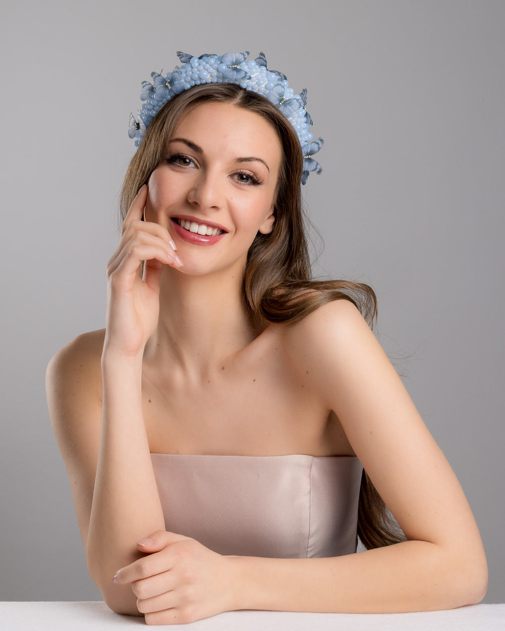 Female model is posing wearing Ice high headband decorated with different sized mat blue beads and scattered blue organza butterflies with crystal centres. Made by Merve Bayindir millinery.