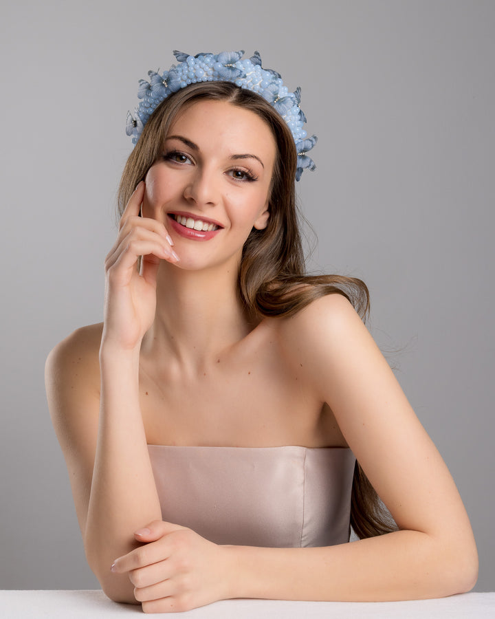 Female model is posing wearing Ice high headband decorated with different sized mat blue beads and scattered blue organza butterflies with crystal centres. Made by Merve Bayindir millinery.