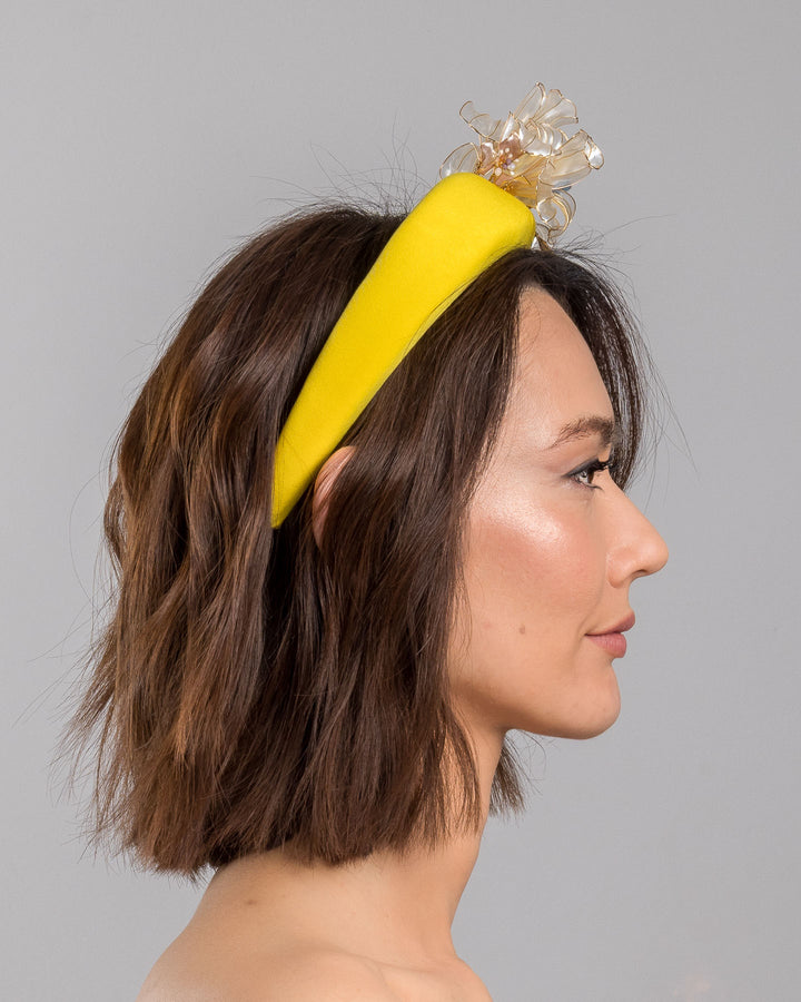Model is showcasing the right side of high yellow headband decorated with wired sheer resin flowers and small metal adornments. Made by Merve Bayindir. 