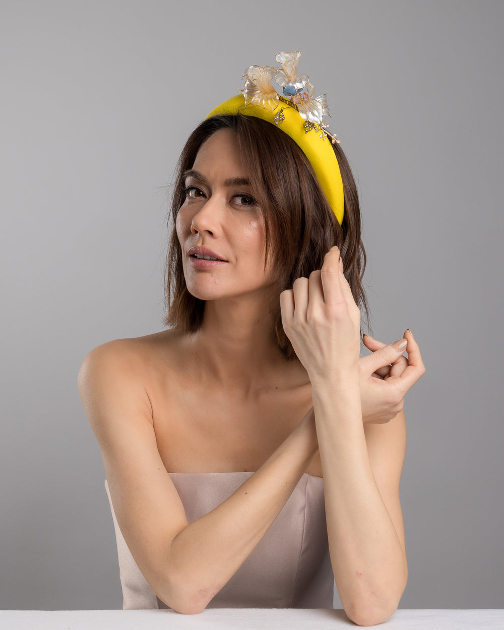 Model is posing wearing Illecebra high yellow headband decorated with wired sheer resin flowers and small metal adornments. Made by Merve Bayindir Millinery.