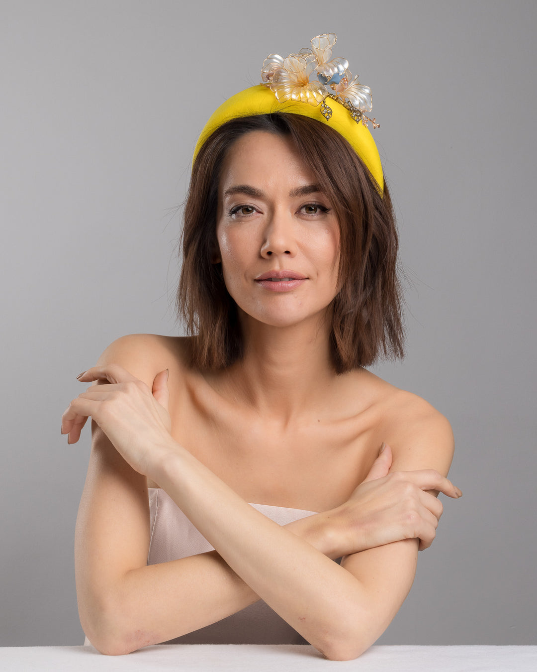 Model is posing wearing Illecebra high yellow headband decorated with wired sheer resin flowers and small metal adornments. Made by Merve Bayindir Millinery.