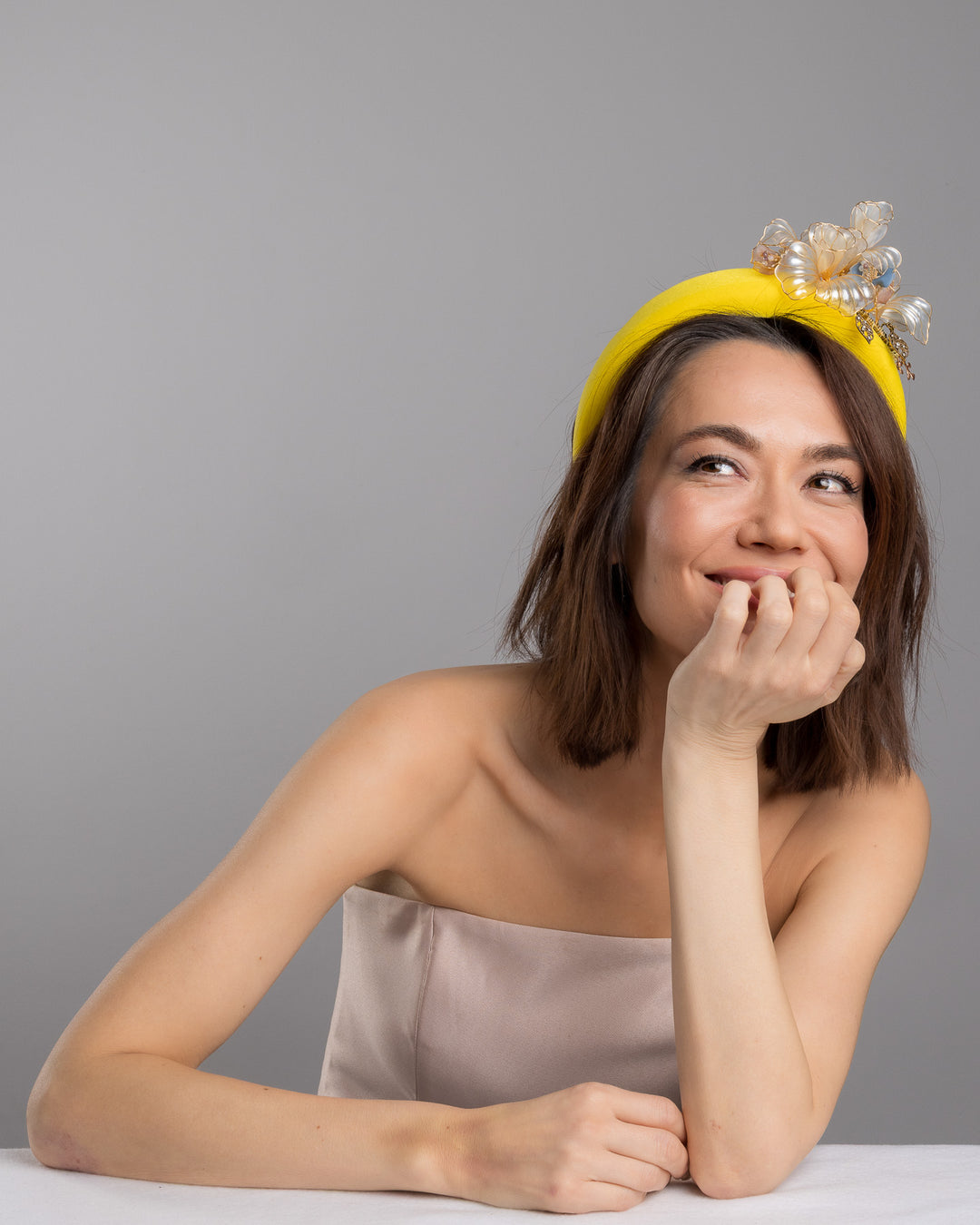 Model is posing wearing Illecebra high yellow headband decorated with wired sheer resin flowers and small metal adornments. Made by Merve Bayindir Millinery.