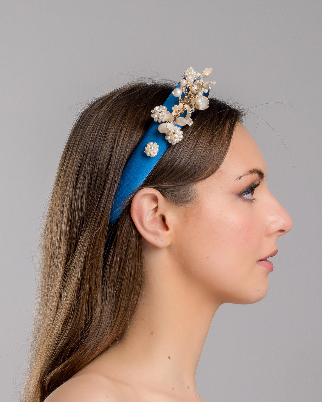 Model is showcasing the right side close up of teal silk sateen headband, a favourite yet hard to find colour decorated with mother of pearl wired flowers as well as mother pearl balls and beads. The pearl on the headband elevates the idea of a simple headband to a whole new level. Made by Merve Bayindir Millinery.