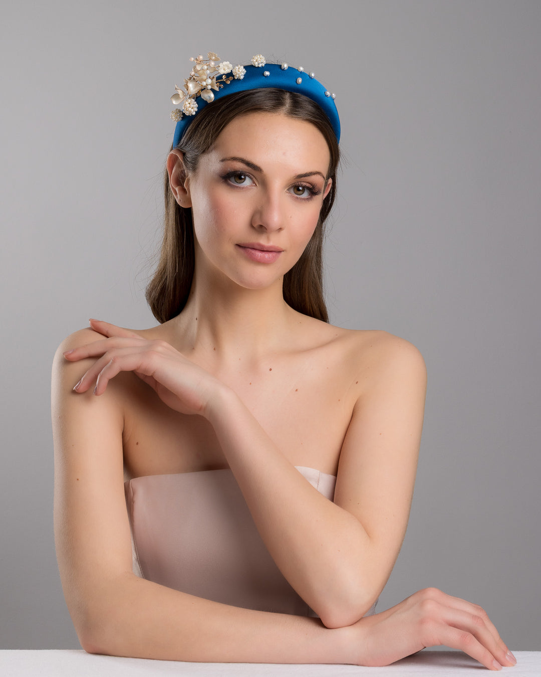 Model is posing wearing IInfatura teal silk sateen headband, decorated with mother of pearl wired flowers as well as mother pearl balls and beads. The pearl on the headband elevates the idea of a simple headband to a whole new level. Made by Merve Bayindir Millinery.