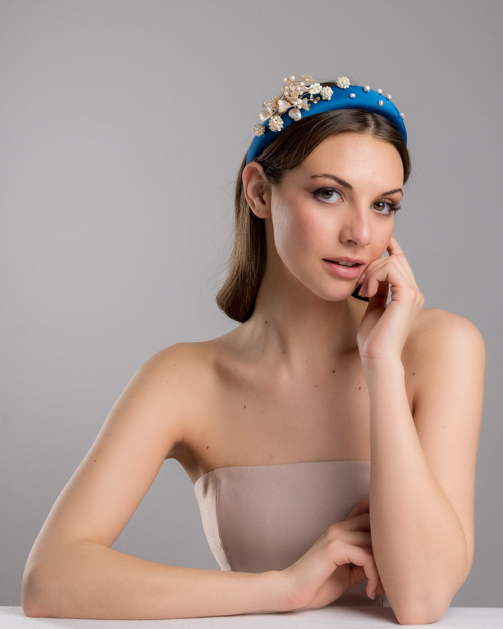 Model is posing wearing IInfatura teal silk sateen headband, a favourite yet hard to find colour decorated with mother of pearl wired flowers as well as mother pearl balls and beads. The pearl on the headband elevates the idea of a simple headband to a whole new level. Made by Merve Bayindir Millinery.
