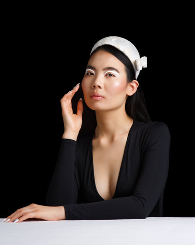 The model is wearing a half moon style white bridal headband decorated with off white sparkle clusters. Adorned with a bow in same detailing on one side.