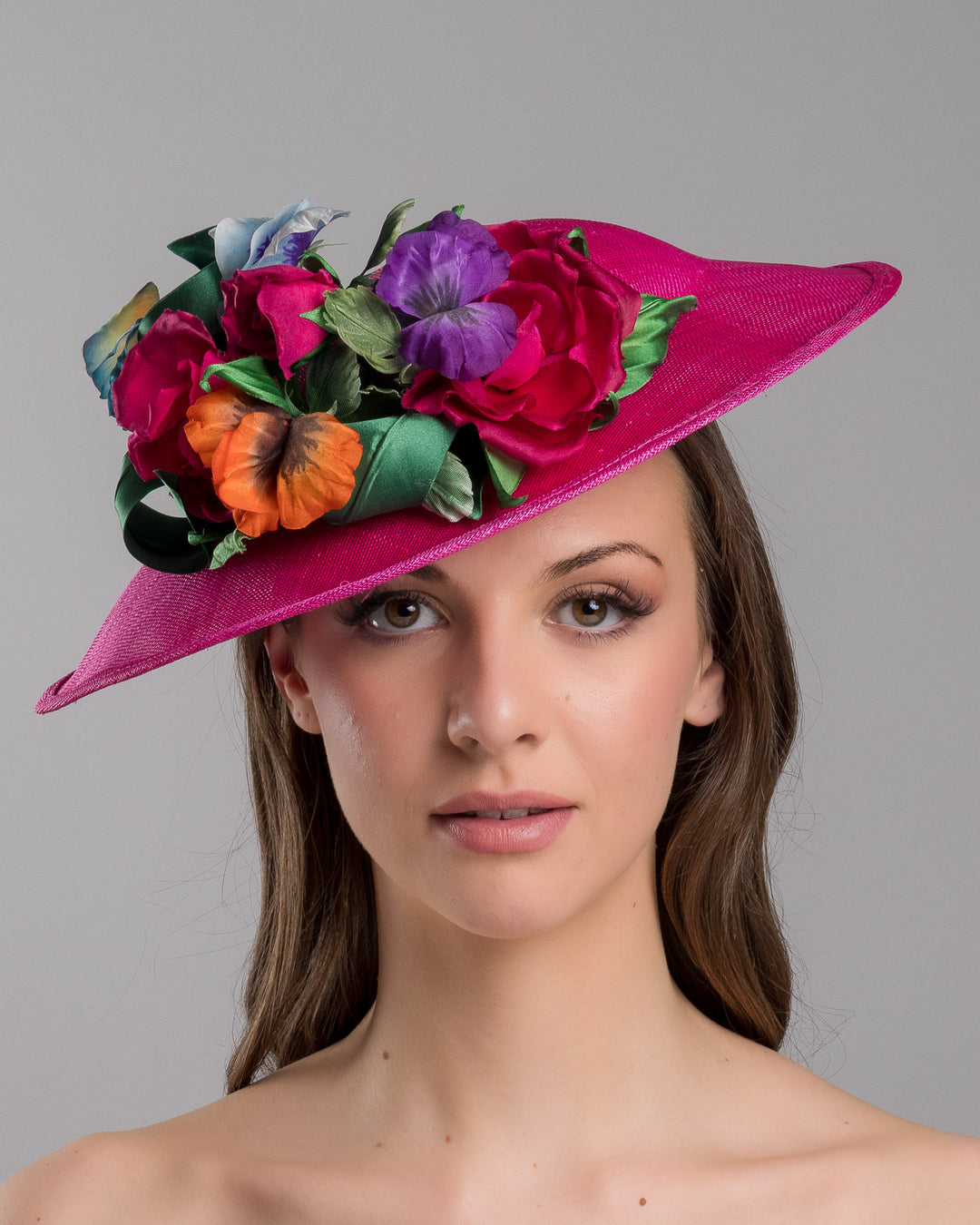 The model is showcasing the front side close up of the medium sized, hot pink medium teardrop saucer decorated with a bouquet of eye-catching pink roses, multi-coloured violets and emerald leaves. Designed and made by Merve Bayindir Millinery.
