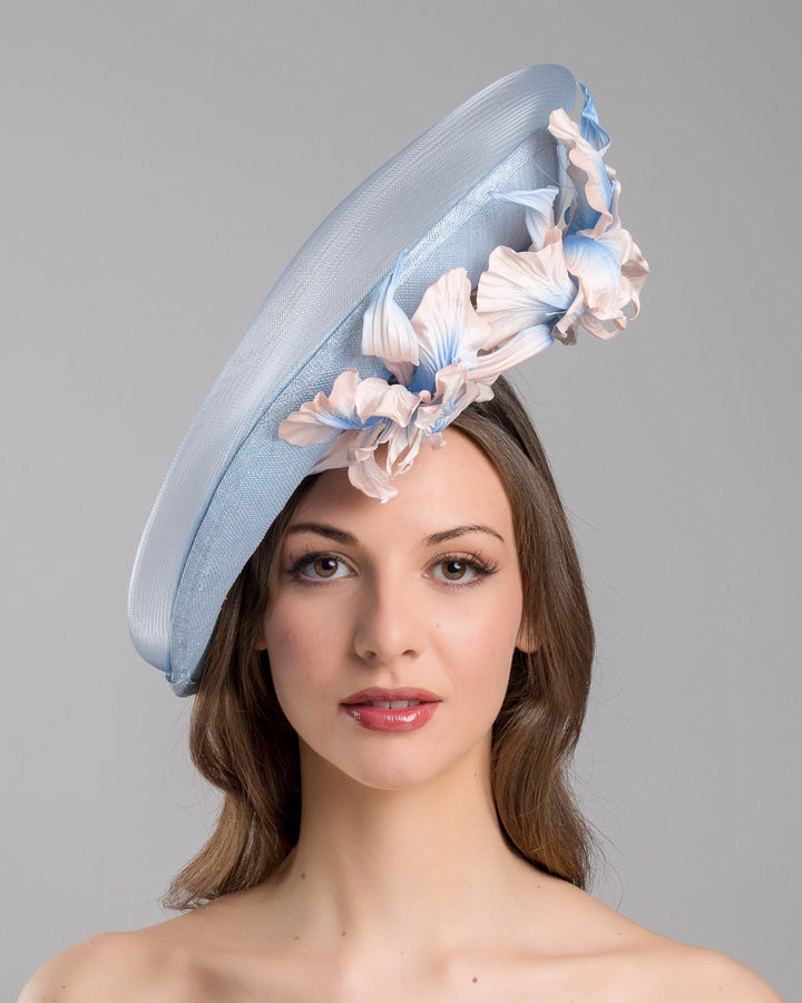 The model is showcasing the front side close up of the medium sized, side saucer shaped light blue headpiece that blends different styles into one. Almost vertical construction of this splendid design softens with a crinoline curve on the left side and features light pink and light blue shaded irises underneath. Designed and made by Merve Bayindir Millinery