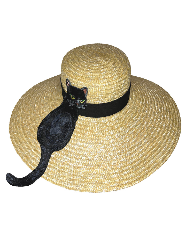 Natural woven wide brim straw boater hat with a wide brim and black grosgrain ribbon band, featuring a large black cat appliqué with green eyes draped over the crown and brim. Design and made by Merve Bayindir Millinery.
