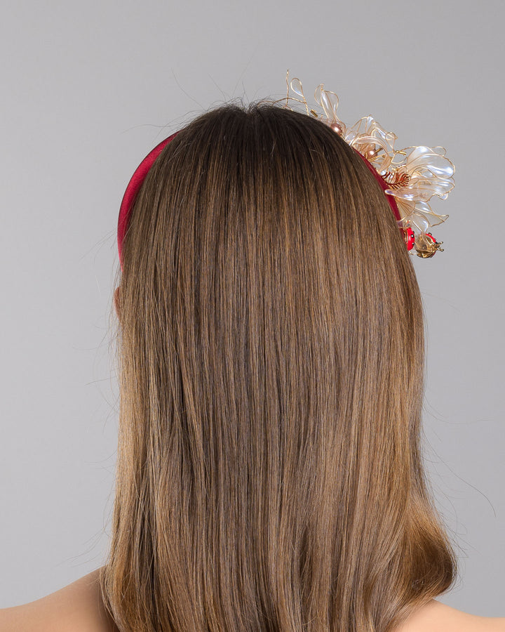Model is showcasing the back side close up of red silk sateen headband decorated with wired resin flowers and lady bug beads. Made by Merve Bayindir Millinery.