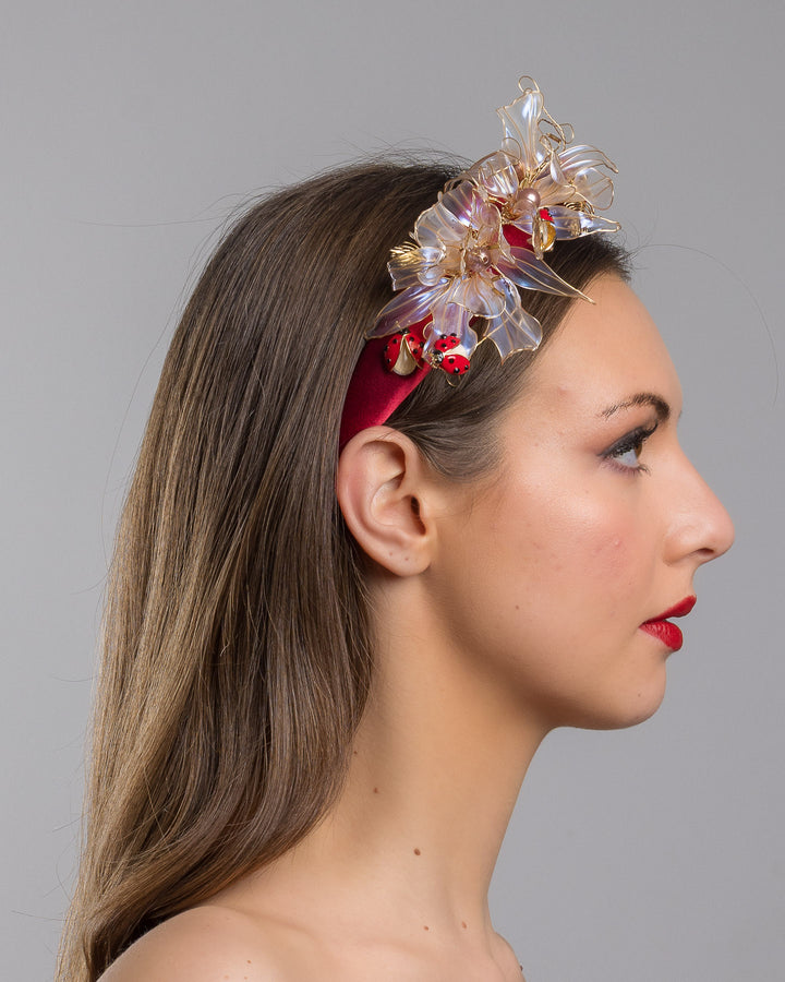 Model is showcasing the right side close up of red silk sateen headband decorated with wired resin flowers and lady bug beads. Made by Merve Bayindir Millinery.