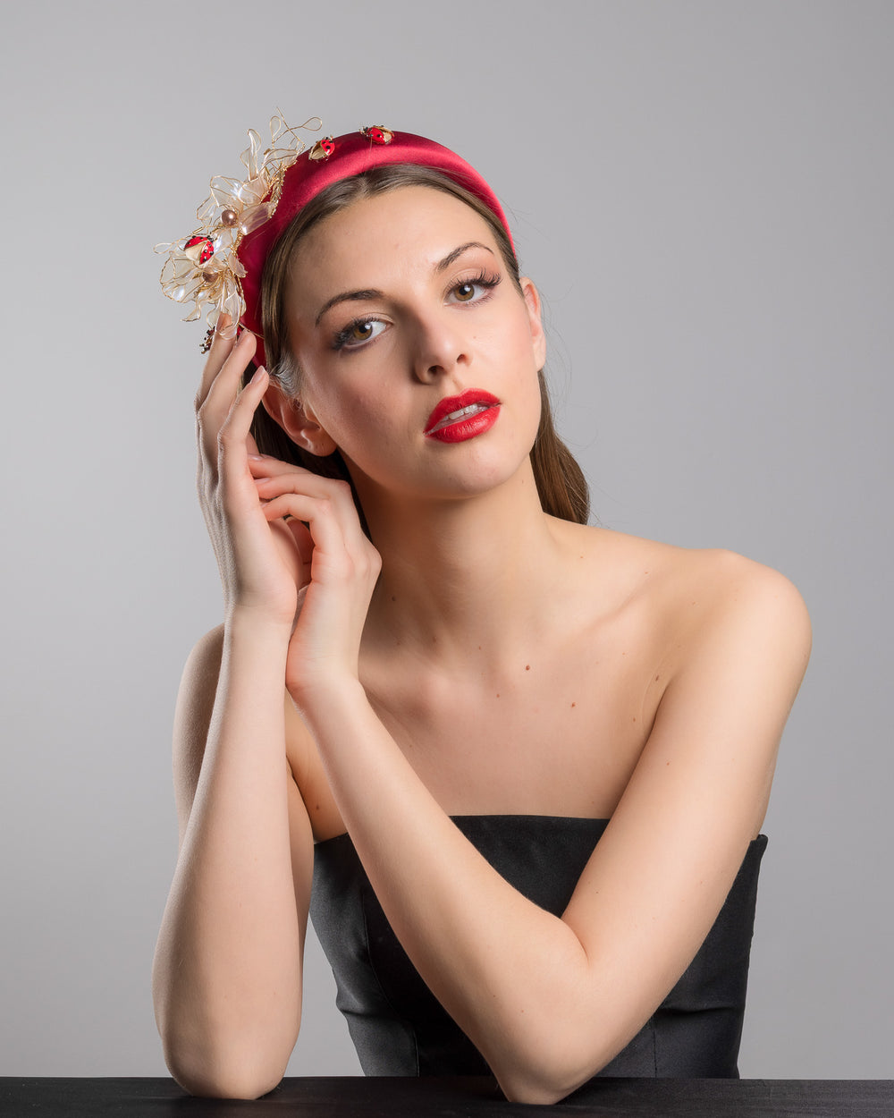 Female model posing wearing Lady Bug red silk sateen headband decorated with wired resin flowers and lady bug beads. Made by Merve Bayindir Millinery.