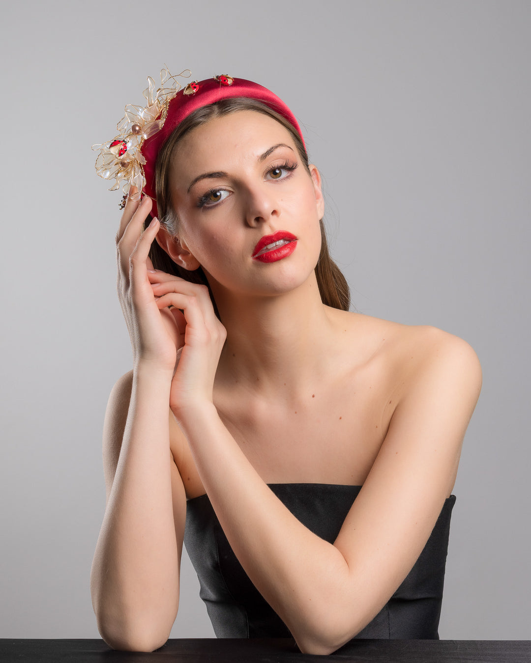 Female model posing wearing Lady Bug red silk sateen headband decorated with wired resin flowers and lady bug beads. Made by Merve Bayindir Millinery.