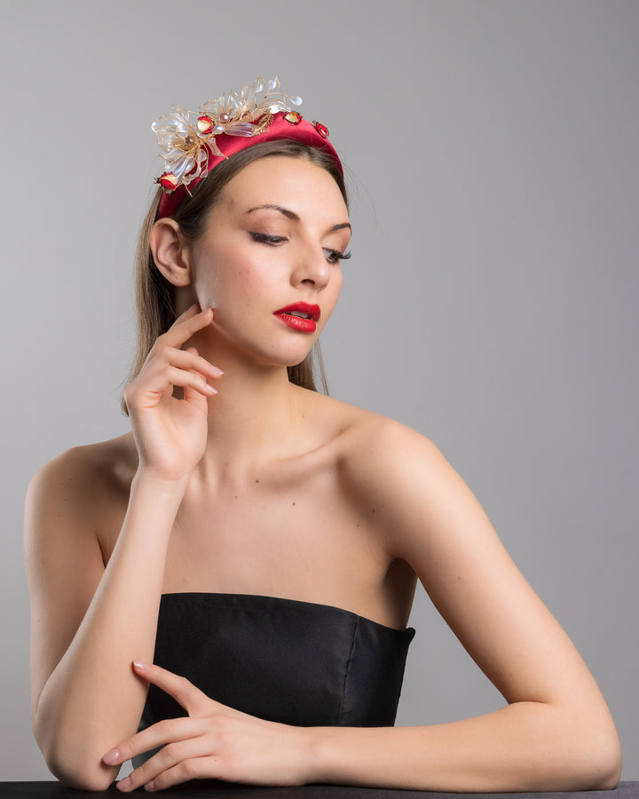 Female model posing wearing Lady Bug red silk sateen headband decorated with wired resin flowers and lady bug beads. Made by Merve Bayindir Millinery.