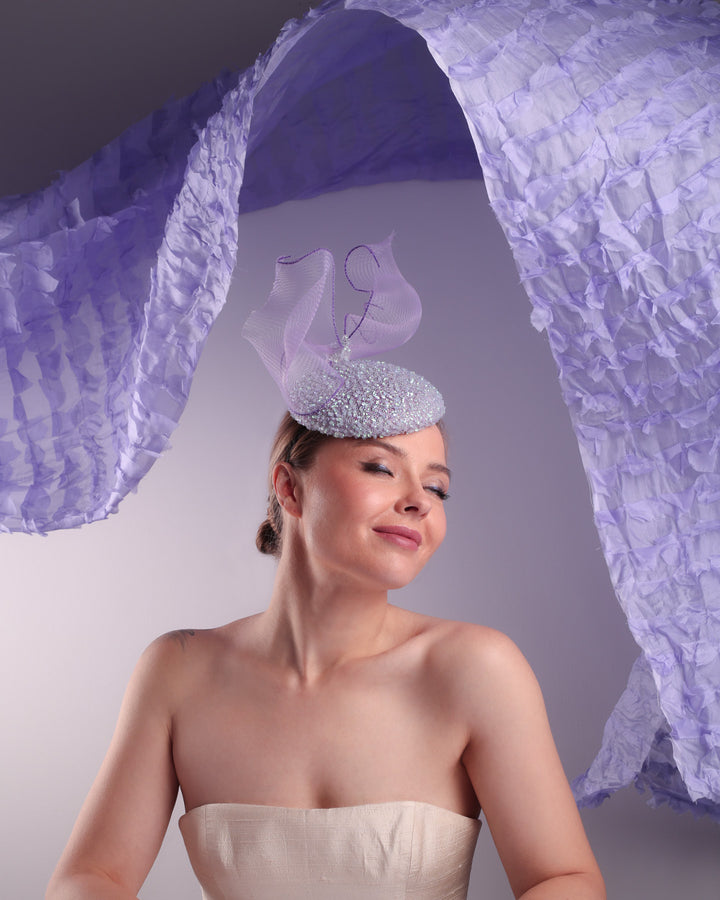 Woman wearing a decorative headpiece with a blue and white feathered design against a textured purple background.