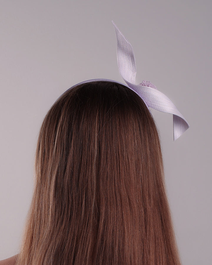 Model is showcasing the back of a silk flat Alice style lilac headband, decorated with a JinSin swirl and a lilac mini tulle ponpon
