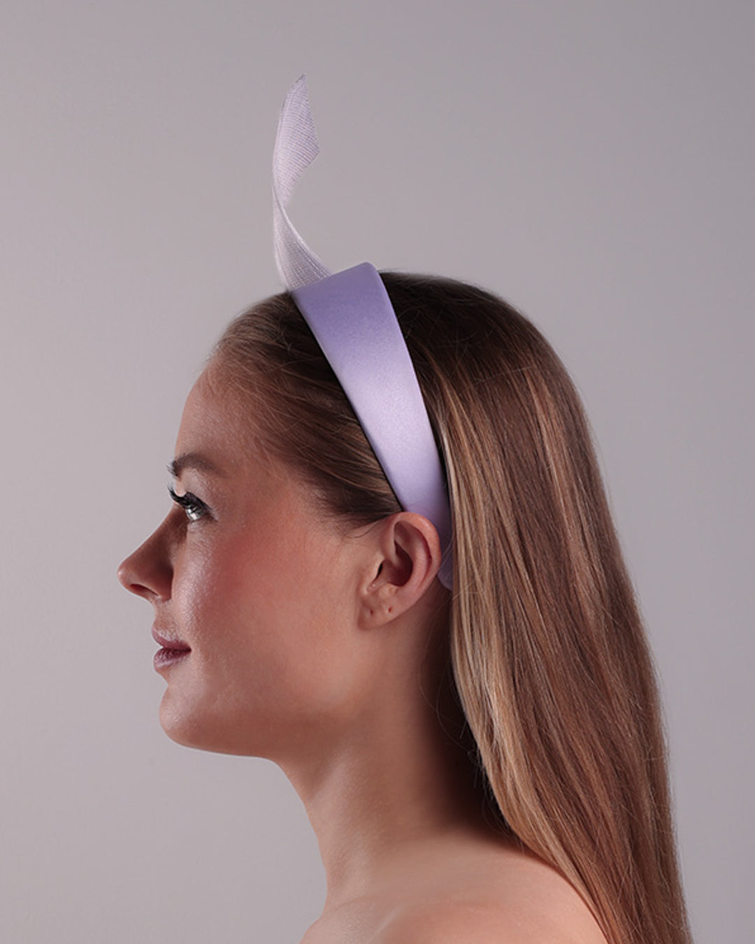 Model is showcasing the left side of a silk flat Alice style lilac headband, decorated with a JinSin swirl and a lilac mini tulle ponpon