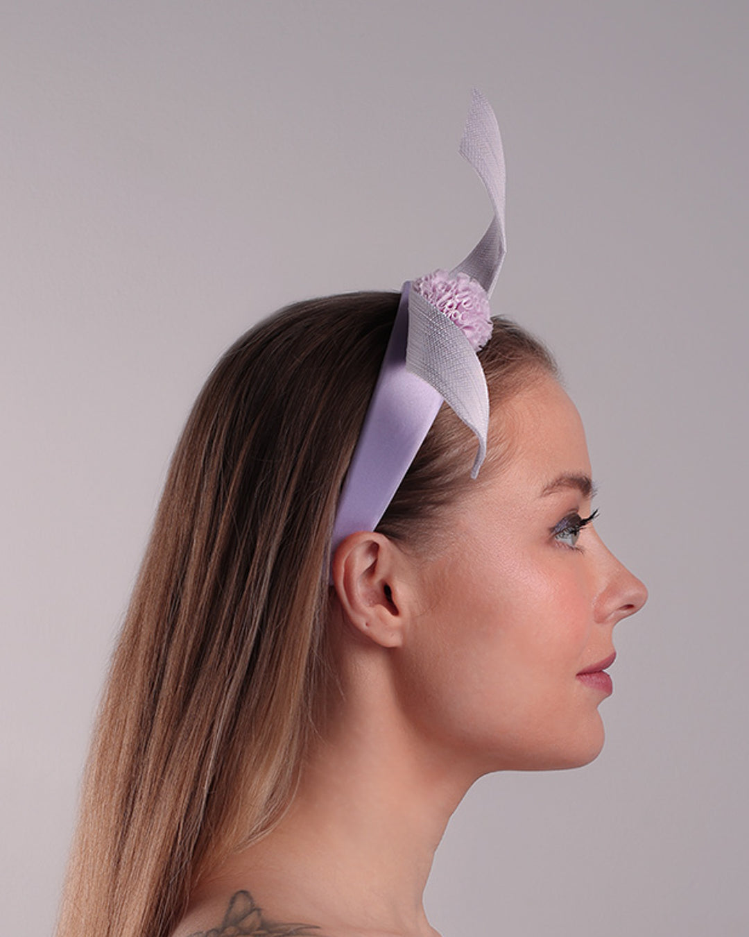 Model is showcasing the right side of a silk flat Alice style lilac headband, decorated with a JinSin swirl and a lilac mini tulle ponpon