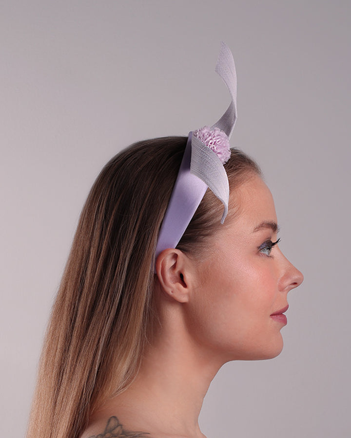 Model is showcasing the right side of a silk flat Alice style lilac headband, decorated with a JinSin swirl and a lilac mini tulle ponpon