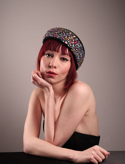 The model showcases the front of the Lumi Beret, crafted in classic black felt, and adorned with multi-coloured crystals that wrap across the front to the side of the brim. Designed by Merve Bayindir.