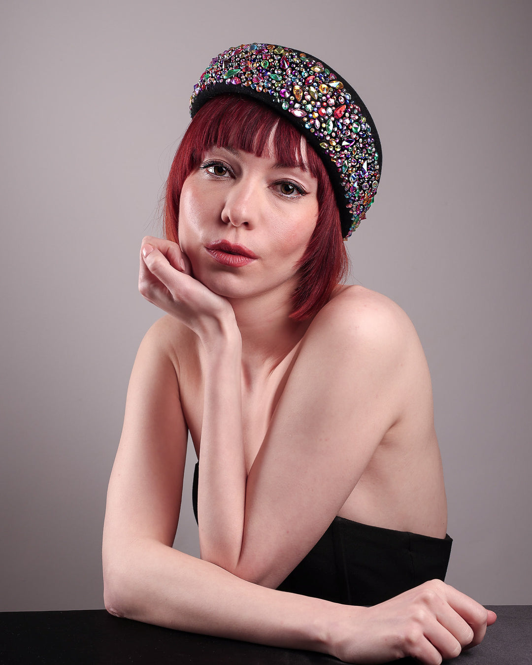 The model showcases the front of the Lumi Beret, crafted in classic black felt, and adorned with multi-coloured crystals that wrap across the front to the side of the brim. Designed by Merve Bayindir.